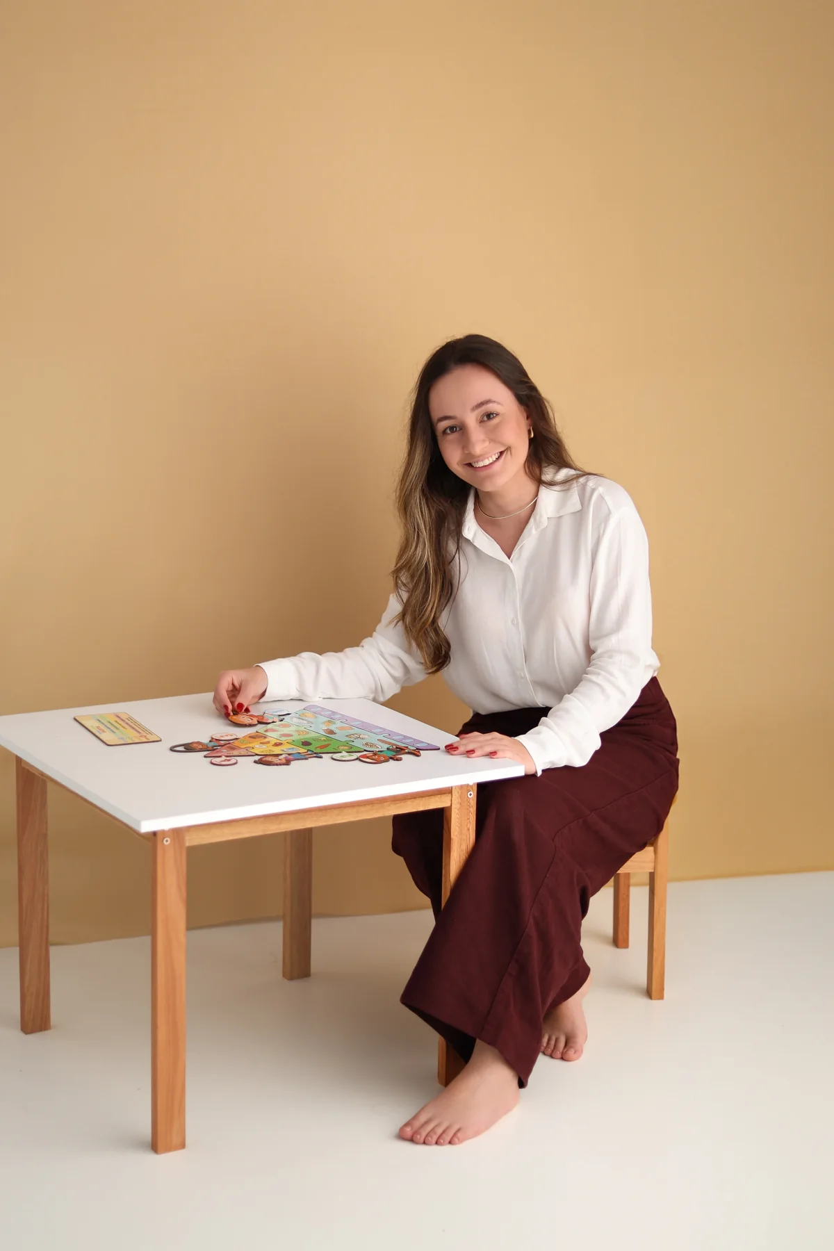 Laura de camisa branca, sentada junto a uma mesa com materiais educativos.